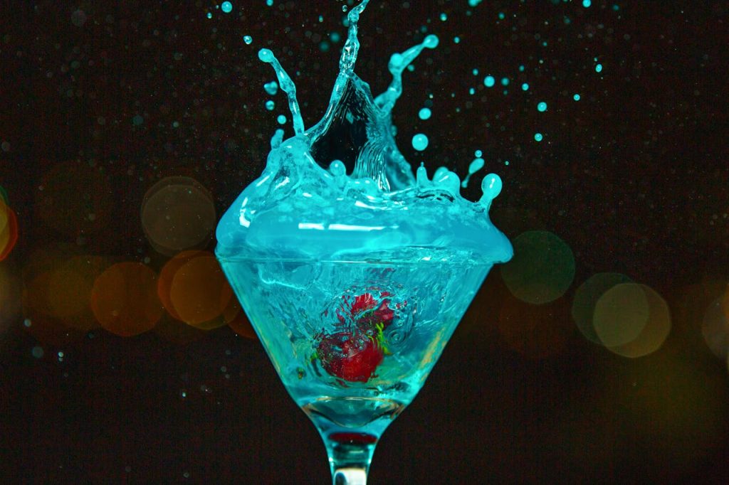 Dynamic splash of a blue cocktail in a martini glass with cherries. Captures motion and vivid colors.