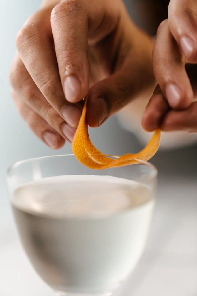 A close-up view of a cocktail being garnished with fresh orange zest.